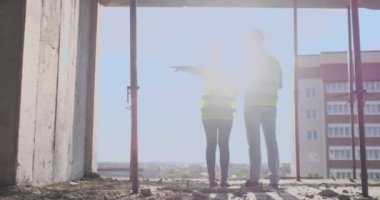 Geri görünüm genç foreman ve mühendis planı kontrol ve inşaat alanında başarı taahhüdü ile inşaat projesi hakkında konuşuyor.