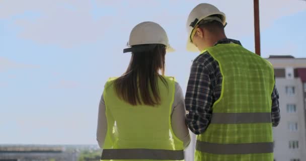 两名工程师或技术员的男子和妇女与安全头盔持有移动无线电话规划建设计划, 以迎接施工现场建设项目, 行业理念. — 图库视频影像