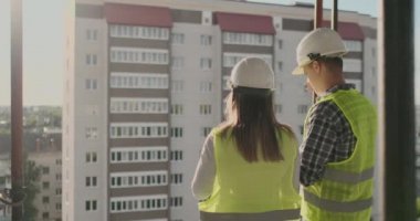 Geri görünüm genç foreman ve mühendis planı kontrol ve inşaat alanında başarı taahhüdü ile inşaat projesi hakkında konuşuyor.