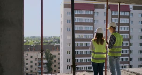 Lavoratori edili che lavorano in cantiere, costruttori che guardano in cianografia, vista posteriore, spazio di copia. Costruzione, sviluppo, lavoro di squadra e concetto di persone — Video Stock