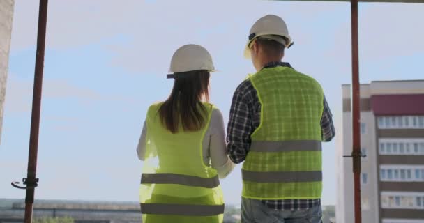 Vista posterior joven capataz e ingeniero revisando el plano y hablando sobre el proyecto de construcción con compromiso con el éxito en el sitio de construcción . — Vídeos de Stock