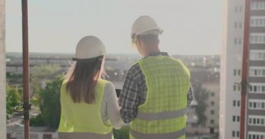 Geri görünüm genç foreman ve mühendis planı kontrol ve inşaat alanında başarı taahhüdü ile inşaat projesi hakkında konuşuyor.