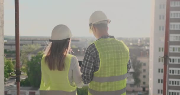 Vista posterior joven capataz e ingeniero revisando el plano y hablando sobre el proyecto de construcción con compromiso con el éxito en el sitio de construcción . — Vídeos de Stock