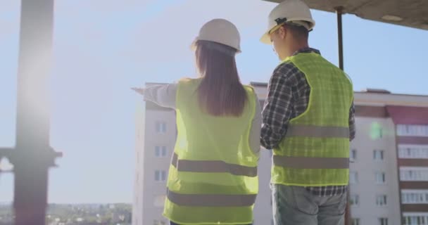 Trabajadores de la construcción que trabajan en el sitio de construcción, constructores que buscan en el plano, vista trasera, espacio de copia. Construcción, desarrollo, trabajo en equipo y concepto de personas — Vídeo de stock