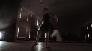 Spot ışıkların önünde yavaşça dans eden bir balerin. Birkaç spot ışığı, yavaş çekimde karanlık bir sahnede dans eden bir balerin gösteriyor..