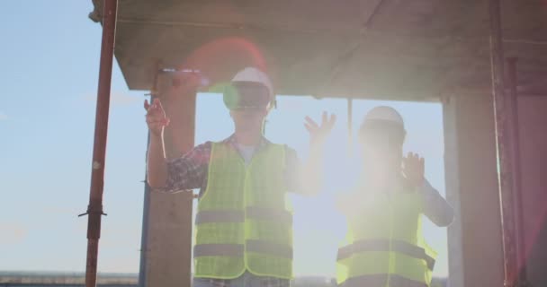 Dos trabajadores contemporáneos de la tripulación usando VR para visualizar proyectos parados en un edificio inacabado en el sitio de construcción, espacio de copia . — Vídeos de Stock