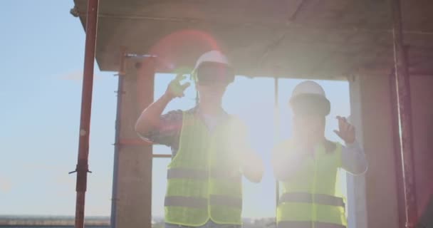 Dos trabajadores contemporáneos de la tripulación usando VR para visualizar proyectos parados en un edificio inacabado en el sitio de construcción, espacio de copia . — Vídeos de Stock