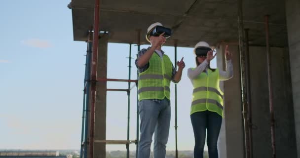 Dos trabajadores contemporáneos de la tripulación usando VR para visualizar proyectos parados en un edificio inacabado en el sitio de construcción, espacio de copia . — Vídeos de Stock