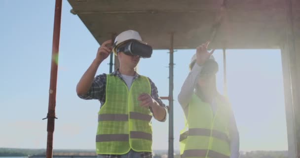 Retrato de cintura hacia arriba de dos trabajadores de la construcción modernos usando equipo VR para visualizar proyectos en el sitio, copiar espacio . — Vídeos de Stock