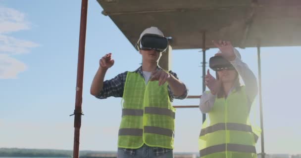 Um homem e uma mulher engenheiros em um canteiro de obras em óculos VR gerenciam a construção de um prédio discutindo um plano de desenvolvimento . — Vídeo de Stock