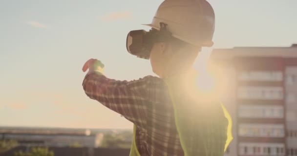 Engenheiro o Construtor no telhado do edifício fica em óculos VR e move suas mãos usando a interface do futuro. Engenheiro futurista do futuro — Vídeo de Stock