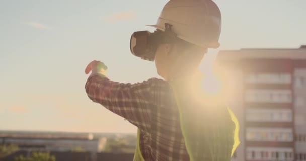 Ingeniero del Constructor en el techo del edificio se encuentra en gafas VR y mueve sus manos utilizando la interfaz del futuro. Ingeniero futurista del futuro — Vídeo de stock