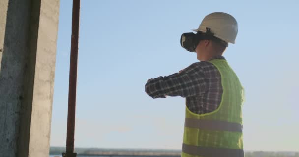 Engineer the Builder on the roof of the building stands in VR glasses and moves his hands using the interface of the future. Futuristic engineer of the future — Stock Video