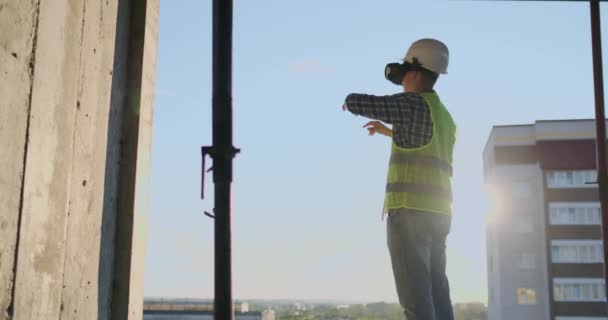 Ingegnere Costruttore visualizza il piano di costruzione in piedi sul tetto dell'edificio al tramonto si erge in VR occhiali e muove le mani utilizzando l'interfaccia del futuro . — Video Stock