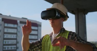 İnşaatçının çatısı üzerinde mühendislik yapımcısı VR gözlük duruyor ve geleceğin arayüzünü kullanarak ellerini taşır. Geleceğin fütüristik mühendisi