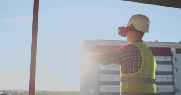 Ingenieur bouwer op het dak van het gebouw bij zonsondergang staat in vr-bril en beweegt zijn handen met behulp van de interface van de toekomst. Futuristische ingenieur van de toekomst. Het uitzicht vanaf de achterzijde. — Stockvideo