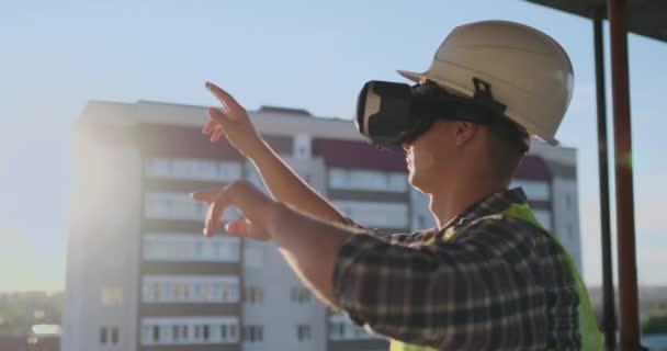 Engineer Builder visualise le plan du bâtiment debout sur le toit du bâtiment au coucher du soleil se tient dans des lunettes VR et se déplace les mains en utilisant l'interface du futur . — Video