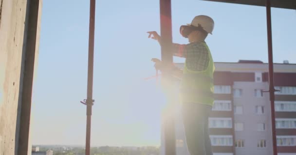 İnşaatçının çatısı üzerinde mühendislik yapımcısı VR gözlük duruyor ve geleceğin arayüzünü kullanarak ellerini taşır. Geleceğin fütüristik mühendisi — Stok video