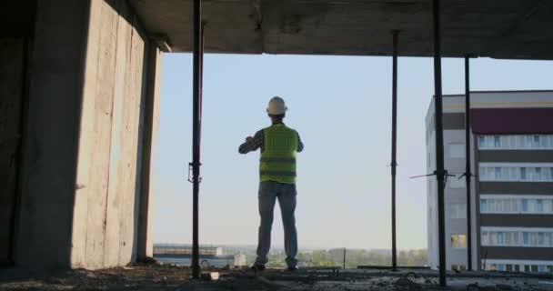 Inżynier budowniczy na dachu budynku o zachodzie słońca stoi w okularach VR i porusza ręce za pomocą interfejsu przyszłości. Futurystyczny inżynier przyszłości. Widok z tyłu. — Wideo stockowe