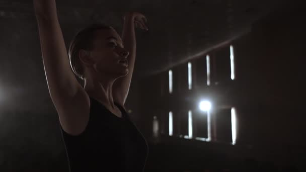 スローモーション:背景に光と煙と暗闇の中で古典的なバレエの要素を踊る勤勉な若い優雅なバレリーナ。暗闇の中で美しい若いバレリーナ — ストック動画