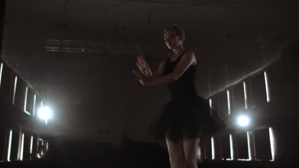 煙の中の劇場の暗いステージに暗いドレスで優雅な女性バレリーナは、スローモーションでダンスの動きを実行します — ストック動画