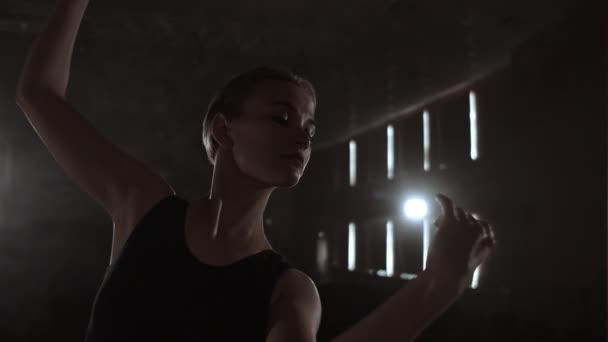 Primer plano de bailarina de ballet mientras practica ejercicios en un escenario o estudio oscuro. Bailarina muestra pasos clásicos de ballet. En cámara lenta. Bengala, disparo de cardán — Vídeo de stock