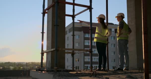Los constructores miran un paisaje urbano sobre un fondo al atardecer, vista trasera — Vídeo de stock