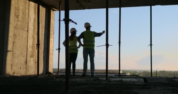 工事現場を見て手に図面を持つ2人のチーフエンジニア。後ろから見る。建設を見て手に青写真を持つチーフエンジニア. — ストック動画