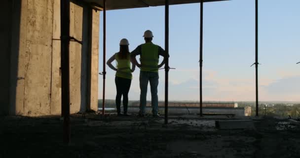 Stavební práce: koncepce spolupráce: mladý inženýr stojící za pohledem na staveniště, s bezpečnostní přilbou. — Stock video