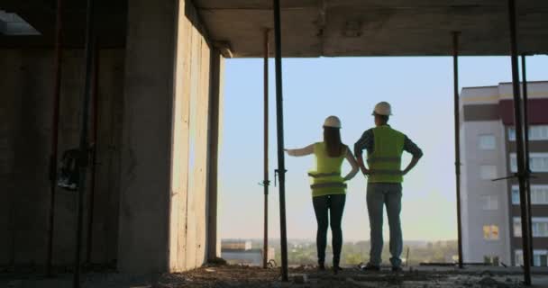 Bouwers kijken een stadsgezicht op een zonsondergang achtergrond, terug weergave — Stockvideo