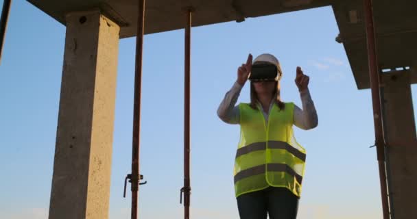 Una ingeniera en una obra de construcción en gafas de realidad virtual mueve sus manos simulando el trabajo de la interfaz del futuro control innovador de la construcción de edificios . — Vídeo de stock