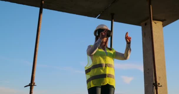 Een vrouw ingenieur op een bouwplaats in virtual reality bril beweegt haar handen simuleren het werk van de interface van de toekomst bij zonsondergang. — Stockvideo