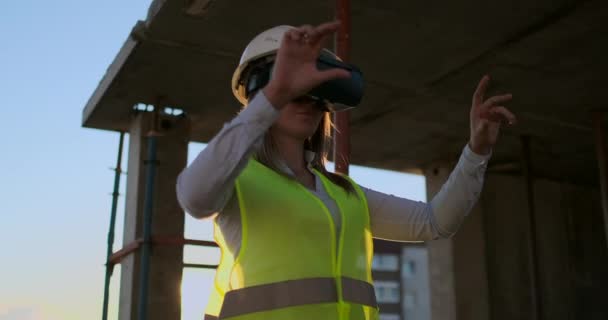 Woman Engineer Builder sur le toit du bâtiment au coucher du soleil se tient dans des lunettes VR et se déplace les mains en utilisant l'interface du futur. Ingénieur futuriste du futur . — Video