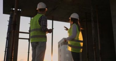 Ofis merkezinde çalışırken koruyucu kask ve yelekler yakışıklı inşaat adam ve kadın işçiler el sallıyor.