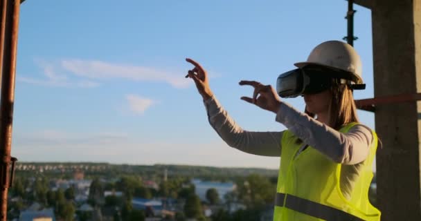 Una donna ingegnere in un cantiere in occhiali realtà virtuale muove le mani simulando il lavoro dell'interfaccia del futuro controllo innovativo della costruzione di edifici . — Video Stock