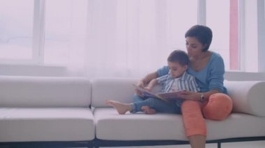 Mutlu anne ve küçük oğlu evde oturma odasında birlikte sabah bir kitap okuma. Aile aktivitesi konsepti