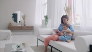 Mutlu bir aile anne ve çocuk oğlu kanepe üzerinde oturan dijital tablet kullanarak, çocuk oğlu ile gülümseyen ebeveyn anne ekran seyir PC bilgisayar online alışveriş yapmak video çağrı izlemek çizgi film yapmak.