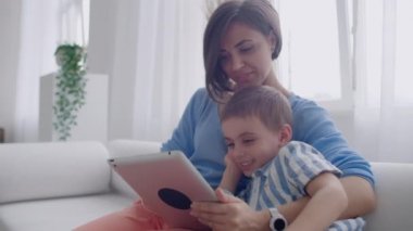 Anne ve oğlu kullanarak tablet ekranına bakarak ve rahat evde kanepe konuşmak.
