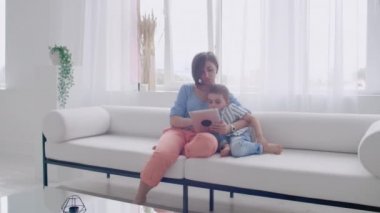 Anne ve oğlu kullanarak tablet ekranına bakarak ve rahat evde kanepe konuşmak.