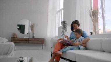 Anne ve oğul kitap okuyor. Mutlu genç anne ve oğlu evde kanepede kitap okumak.