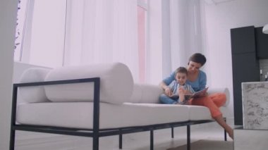 Anne ve oğul kitap okuyor. Mutlu genç anne ve oğlu evde kanepede kitap okumak.