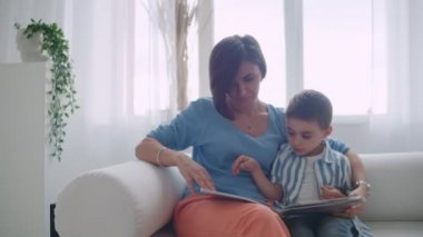 Kanepede oturma odasında evin parlak beyaz iç oturan bir kitap okuma bir çocuk ile genç bir anne.