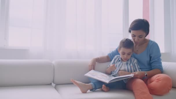 Lycklig mor och barn son läsning bok skrattar i sängen. Lycklig familj mor och barn son Reading Holding bok ligger i sängen, leende mamma barnvakt. — Stockvideo