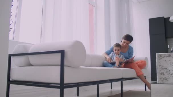 Moeder en zoon lezen boeken. Gelukkige jonge moeder en zoon lezen boeken op de Bank thuis. — Stockvideo