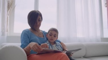 Sevgi dolu bir anne oğlu evde kanepede konuşma holding kitap okumak için öğretim.