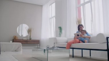 Mutlu bir aile anne ve çocuk oğlu kanepe üzerinde oturan dijital tablet kullanarak, çocuk oğlu ile gülümseyen ebeveyn anne ekran seyir PC bilgisayar online alışveriş yapmak video çağrı izlemek çizgi film yapmak.