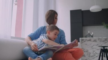 Anne ve oğul kitap okuyor. Mutlu genç anne ve oğlu evde kanepede kitap okumak.