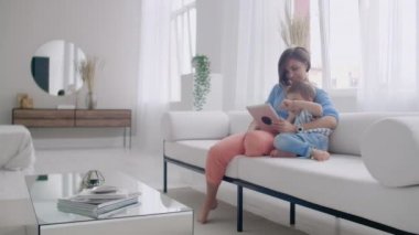 Anne ve oğlu kullanarak tablet ekranına bakarak ve rahat evde kanepe konuşmak.