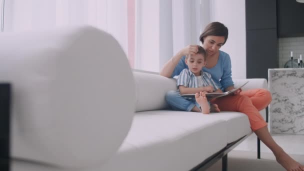 Retrato de niño lindo leyendo libro con la madre mientras está sentado en la caja fuerte . — Vídeo de stock