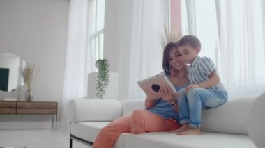 Anne ve oğlu dijital tablet kullanarak koltukta oturuyor. Tablet dokunmatik ekranlı bir video izlerken birlikte mutlu anne ve küçük çocuk kullanarak. Gülümseyen anne ve sevimli çocuk dijital tablet üzerinde oynama